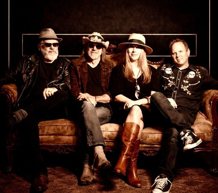 Dirt Road Opera band members sitting on a vintage sofa, performing at Friday Night Live event.